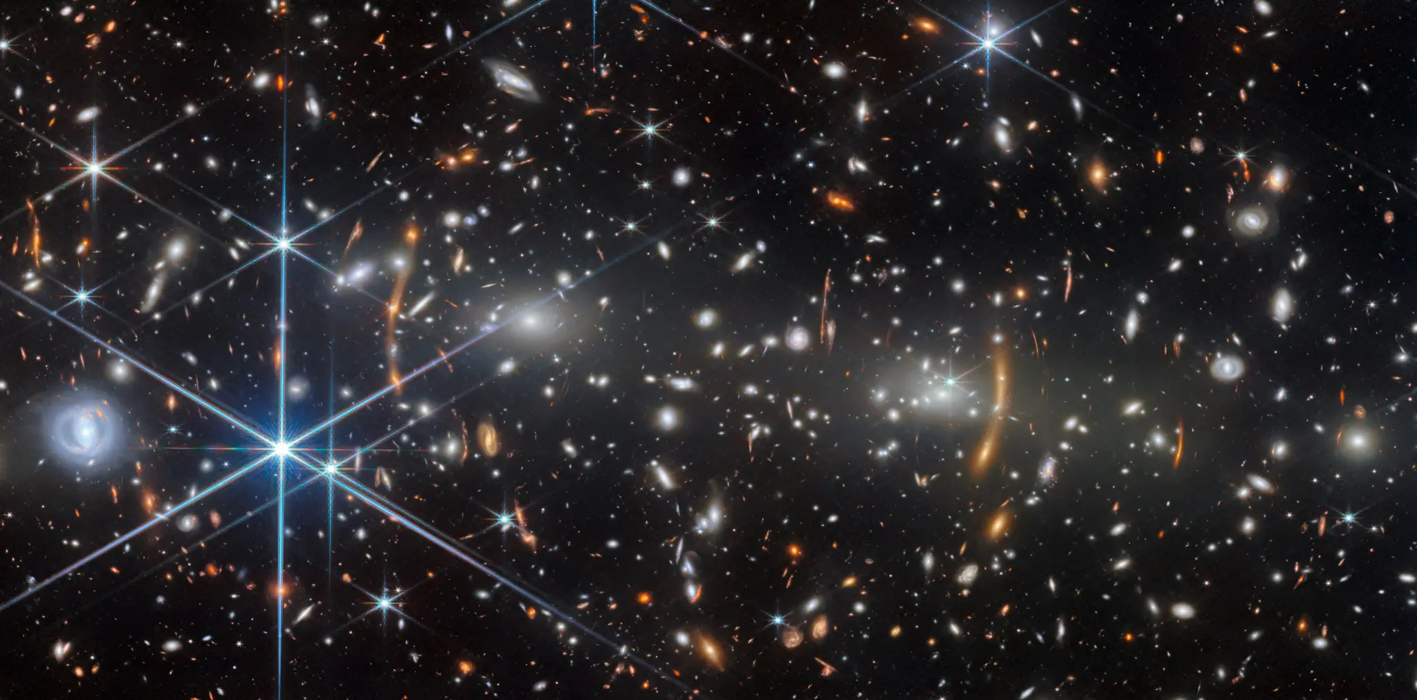 Webb view of the young galaxy cluster MACS J0553.4-3342, filled with bright galaxies and orange arcs created by gravitational lensing